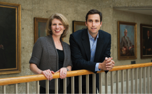 Photo of Nora and David, side-by-side, smiling and leaning on the stair rail on the second floor of Robert Crown Law Building.