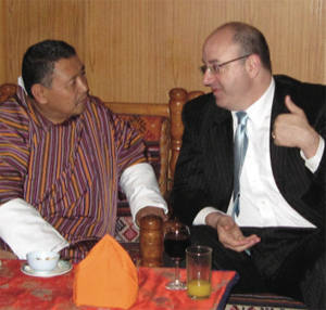 Photo of Dean Kramer seated with a Bhutanese man at a table, deep in conversation.