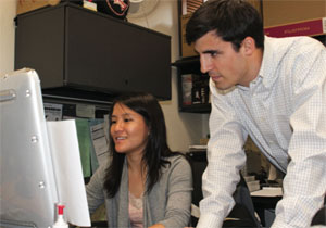 Wells and Wu work at a computer in an office.