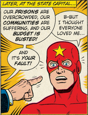 A panel from a superhero comic. The background text reads, "Later, at the state capital...", a finger points at Captain Lock-Em-Up, a masked superhero, accusing "Our prisons are overcrowded, our communities are suffering, and our budget is busted! And it's your fault!". Bewildered the superhero defends, "But I thought everyone loved me..."