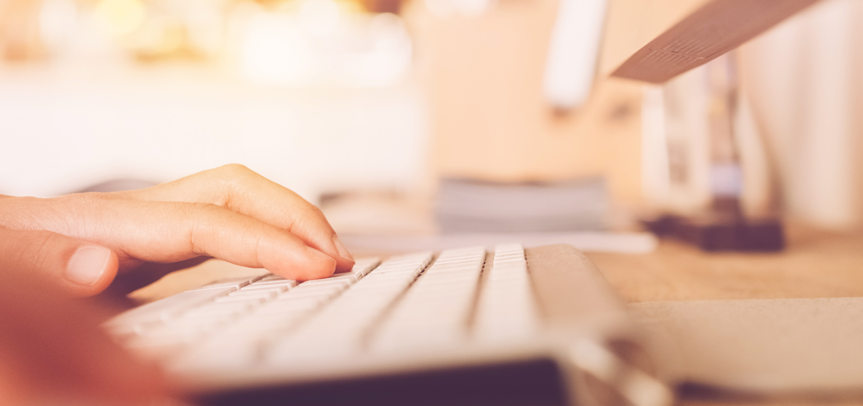 Photo of a person at a computer; closeup of their hands at the keyboard.