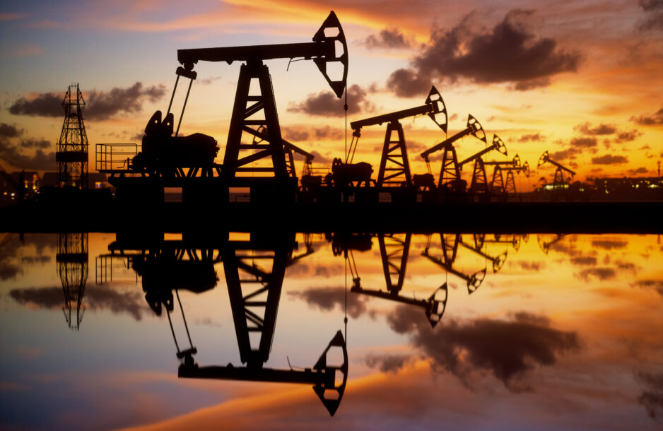 Pump jack silhouette against a sunset sky with reflections in the water.