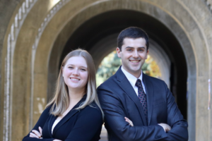 Victoria Gardner and Greg Schwartz in suits standing before an arch