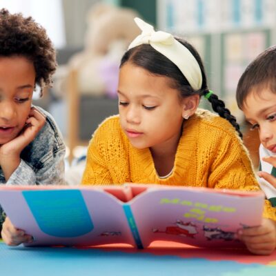 Three young elementary school kids reading a book together.