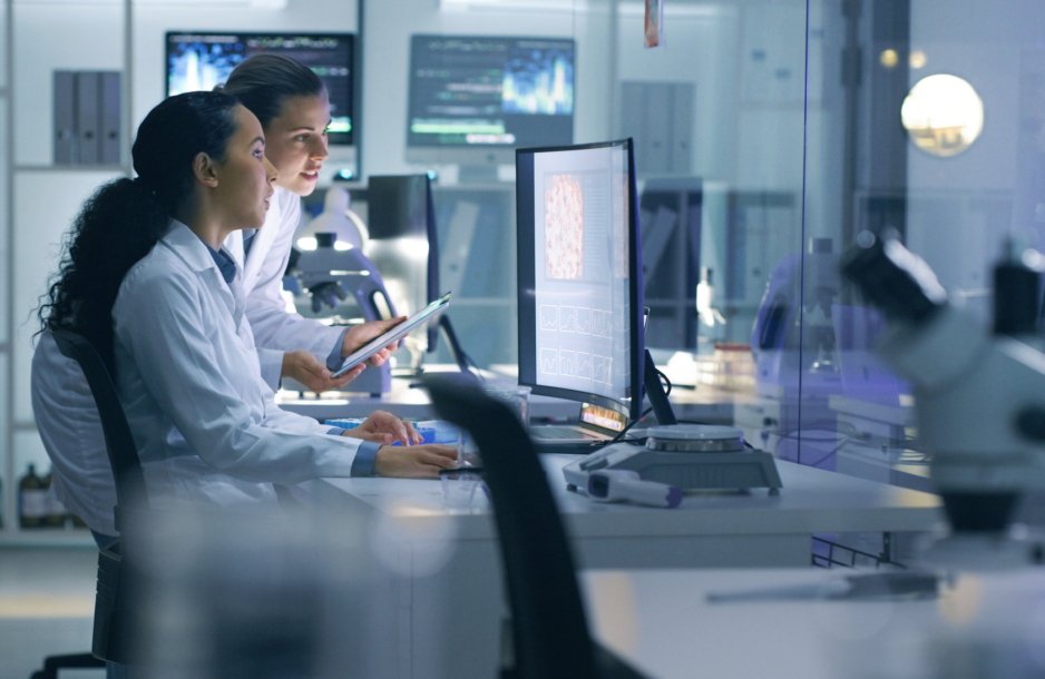 Focused, serious medical scientists analyzing research scans on a computer, working late in the laboratory. Lab workers examine and talk about results from a checkup while working overtime